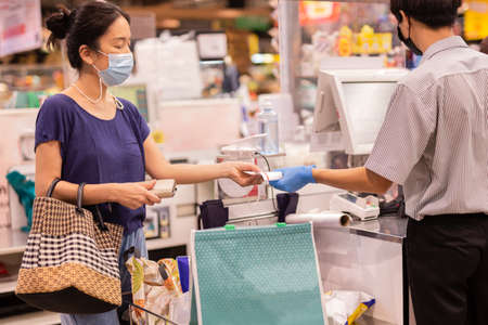 Woman with medical mask taking receipt from male cashier at supermarket.の写真素材