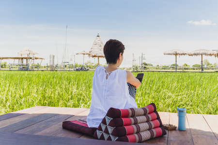 Woman sit on wooden floor looking at cell phone with nature landscape view.の写真素材