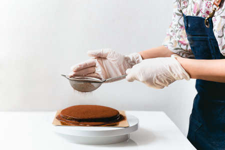 Woman wearing apron powdering chocolate cake with cocoa powder.の写真素材