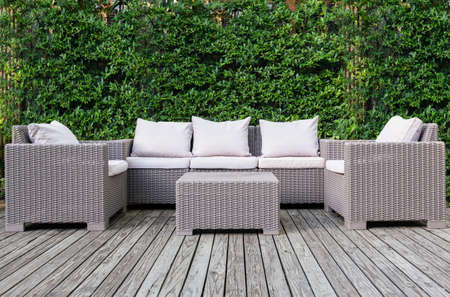 Beautiful wooden terrace with rattan garden furniture with greenery background.