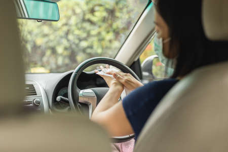 Woman in medical mask cleaning hands with wet wipes while sitting in her car.