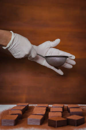 Woman hand with glove adding cacao powder on fresh nama chocolate.の写真素材