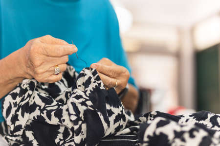 Elderly woman hands using needle and thread to mend a dress.