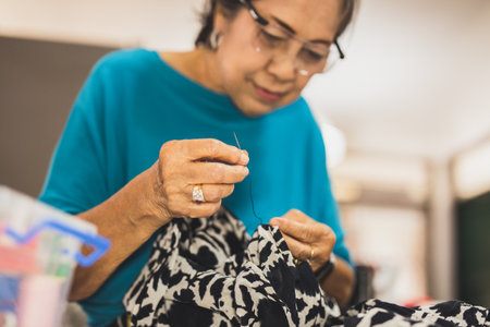 Elderly woman hands using needle and thread to mend a dress.