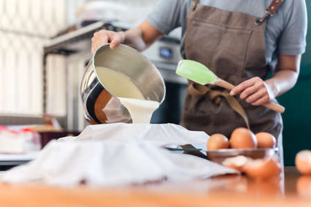 Woman hands pouring cake batter into cake mold.