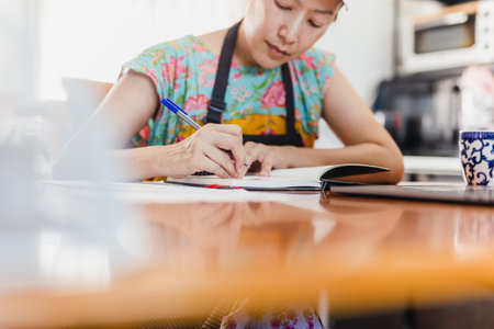 Baker woman in apron work at table write down recipe indoor.の写真素材