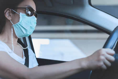 woman driving car with medical mask and sunglasses on her face. Health care and virus protection.の写真素材