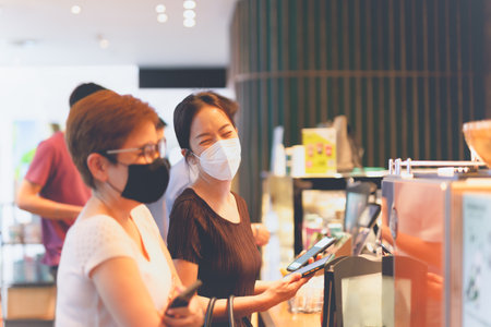 Two happy female friends in protective mask buying coffee.の写真素材