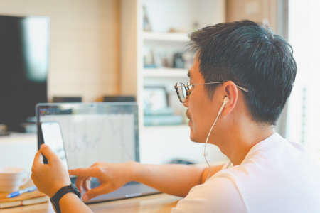 Business man trader using mobile phone app and laptop analytics for financial stockmarket at home.の写真素材