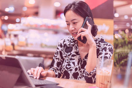 Attractive woman talking on mobile phone while working on laptop sitting in coffee shop.