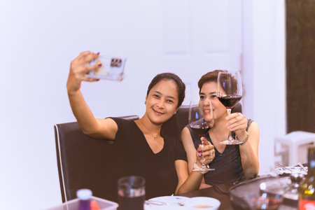 Beautiful women taking a selfie from mobile phone while having glasses of red wine in the house.