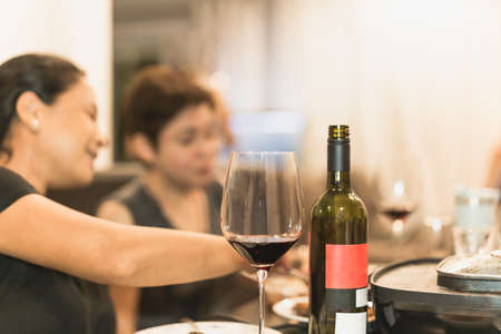 Wine bottle and glasses on dinner table with woman in background.の写真素材