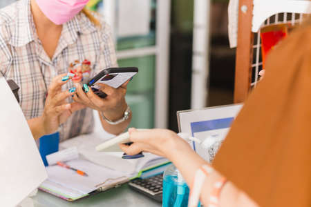Female customer in protective mask make contactless mobile payment sales woman in retail shop.の写真素材