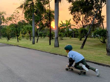 Asian young child learning to skateboard outdoor in the park at sunset.