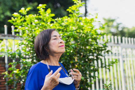 Senior woman holding protective mask in her hand standing in the garden for fresh air.の写真素材