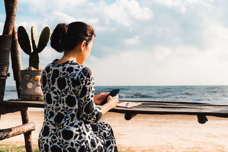 Woman sit at table using smart phone on the beach.の写真素材