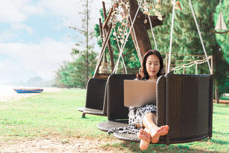 Beautiful woman working laptop while sitting in hammock on the beach .