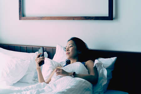 Woman relaxing in bed making video call on smart phone in the morning.の写真素材