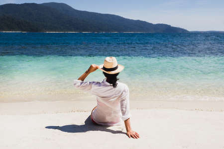 Summer lifestyle of woman wearing straw hat sitting on the beach in tropical island.の写真素材
