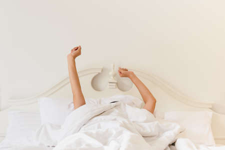 Woman in bed under the blanket stretching hand after waking up.