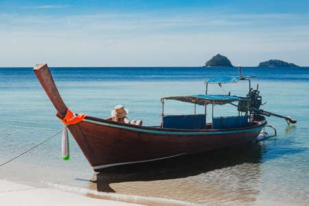 Unidentified woman sitting on a wooden boat in the sea sun bathing.の写真素材