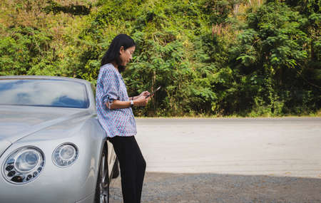 Woman traveler standing next to car trying to get signal on mobile phone.の写真素材