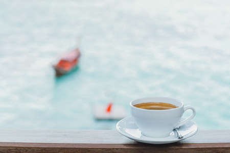 Coffee cup on wooden top with ocean view in background.の写真素材