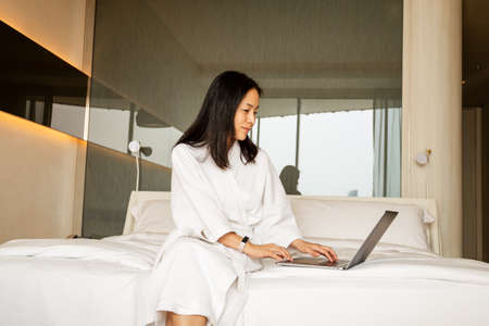Woman sitting on the bed in dressing gown working laptop.の写真素材