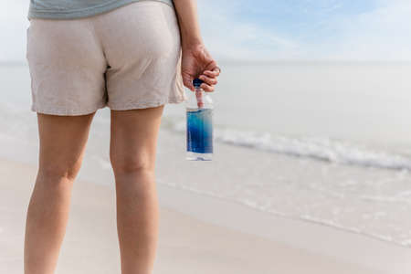 Woman in short standing on the beach holding bottle of water.の写真素材