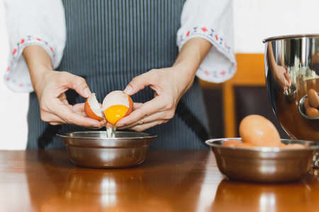Female baker with apron cracking an egg prepare for baking on wooden tableの写真素材