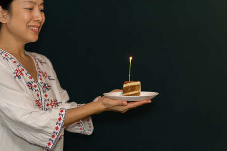 Woman hand holding a piece of birthday cake on the plate with candle.の写真素材