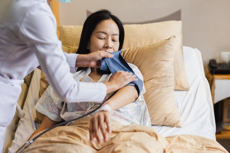 Nurse taking mature female patient blood pressure In hospital bed.の写真素材