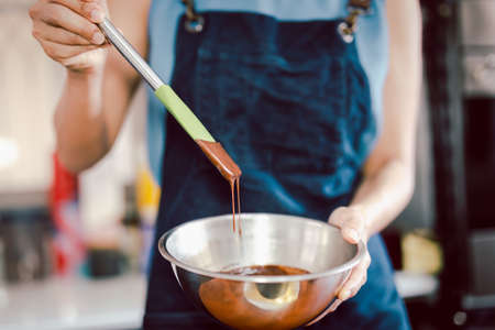 Woman mixing smooth delicious dark chocolate ganache with whisk in silver bowl.