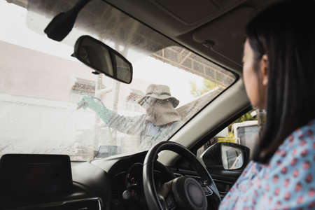 Worker washing car on carwash station outdoor using high pressure water.