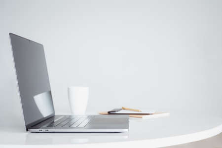 Open laptop computer with coffee and notebook on white table.