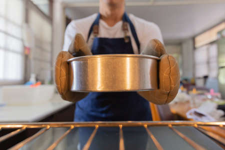 Male baker take cake out of a hot oven