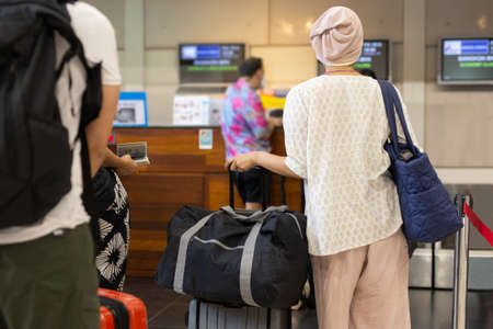 Asian woman tourist standing with luggage at check in counter in airport terminal.