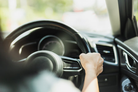 Close up of woman driving hand holding steering wheel in blur background.