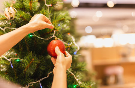 Womans hand hang a Christmas red ball on Christmas tree decoration festive mood.の写真素材