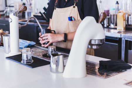 Lady barista in apron preparing and steaming milk for coffee in cafe.の写真素材
