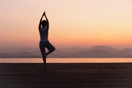 Full length rear view of woman standing on one leg while doing yoga at sunrise.の写真素材