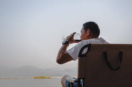 Man sitting on a chair and drinking red wine by the lake.の写真素材