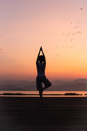 Full length rear view of woman standing on one leg while doing yoga at sunrise.の写真素材