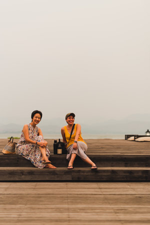 Two women friends sitting on wooden deck with happy smiling.の写真素材