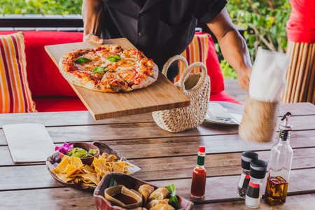 Pizza on a wooden board is serving by a waiter.の写真素材