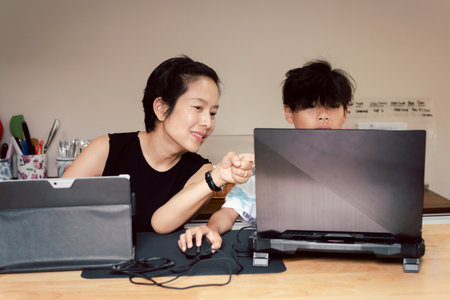 Mother and son working on laptop together in kitchen at home.