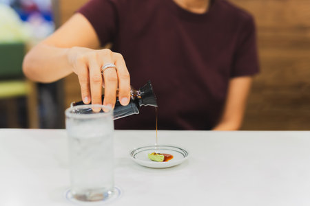 Woman customer hand pouring Japanese soy sauce on wasabi in small plate.の写真素材