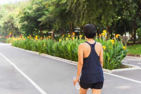 Back view of woman exercise walking in the park with hand holding bottle water