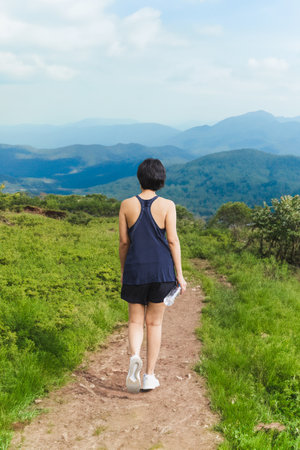 Woman exercise walking on hillside trail with mountain view.の写真素材