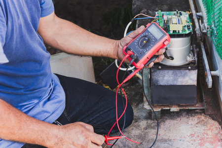 Electrician checking mainboard with multimeter outdoors at homeの写真素材
